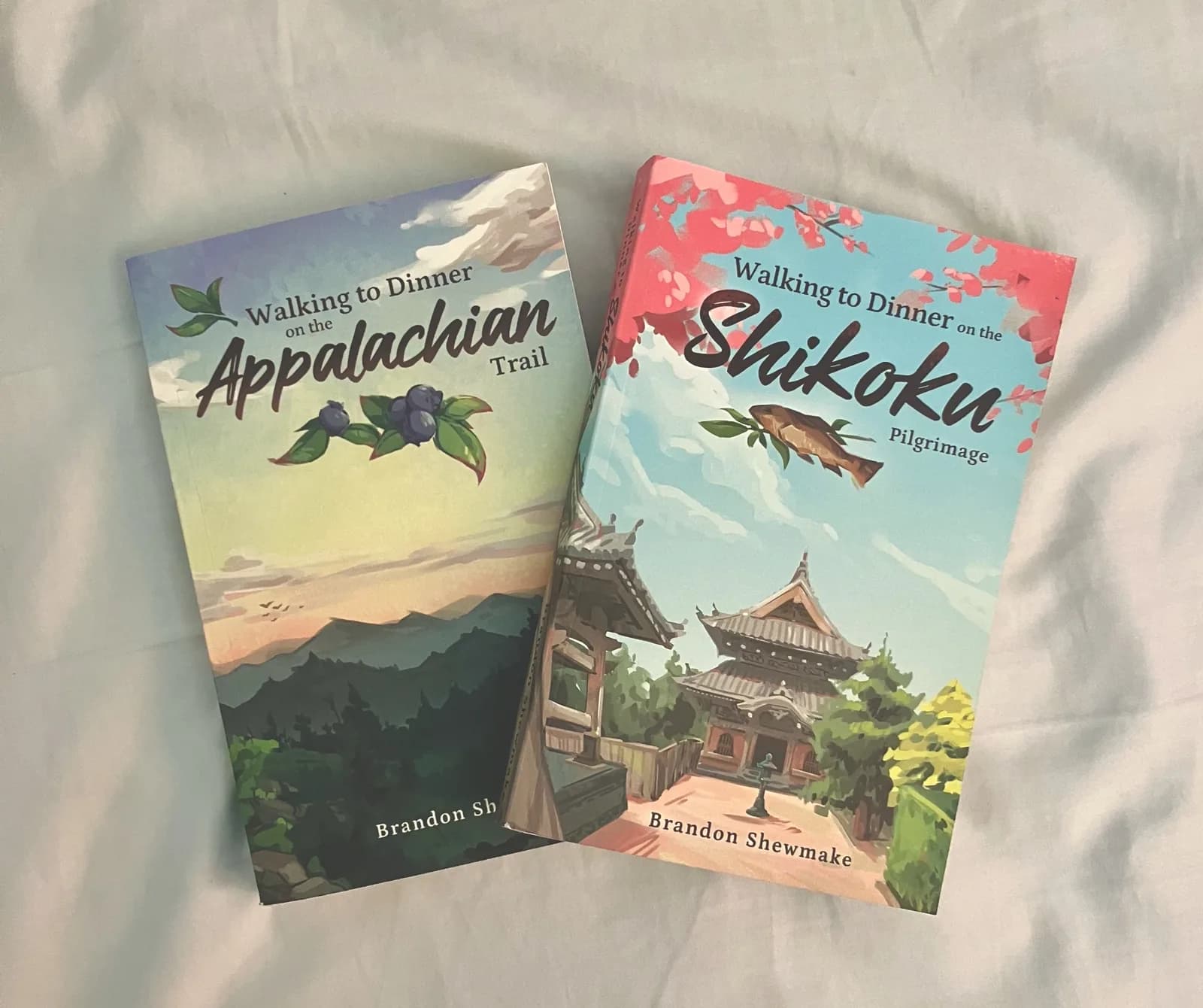 Photo of printed paperback copies of 'Walking to Dinner on the Appalachian Trail' and 'Walking to Dinner on the Shikoku Pilgrimage' by Brandon Shewmake, lying side by side